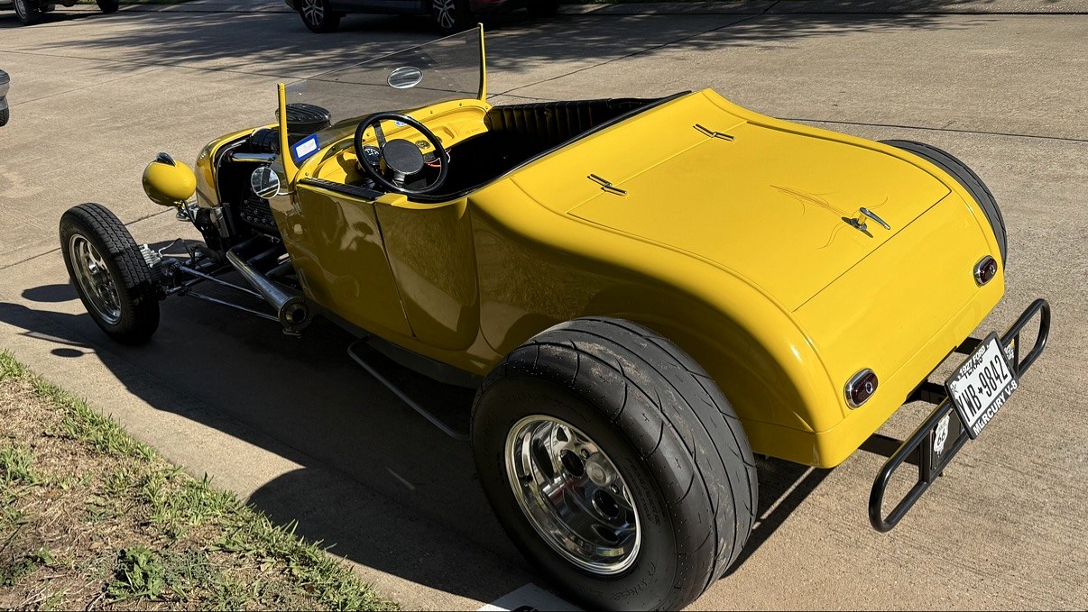 Yellow T-bucket hot rod, exposed chrome engine, open cockpit and wide rear tires